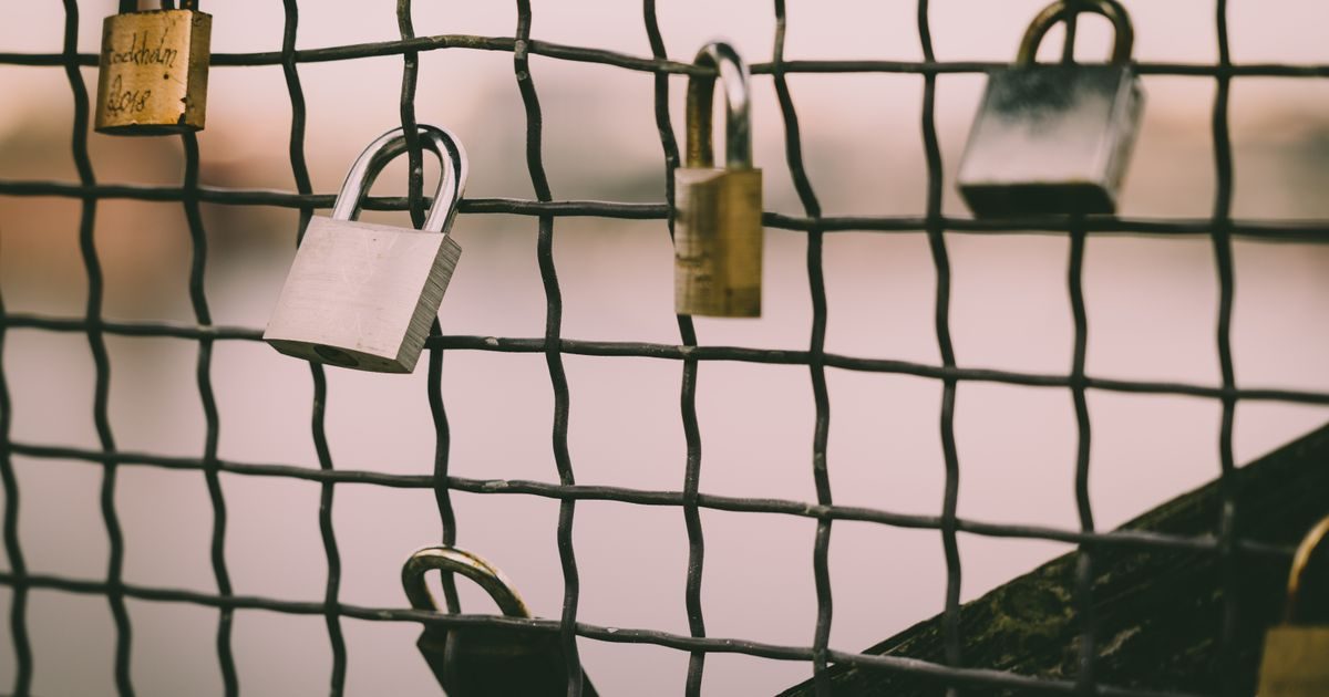 Close-up of romantic love padlocks hanging on a metal wire mesh fence by a river.