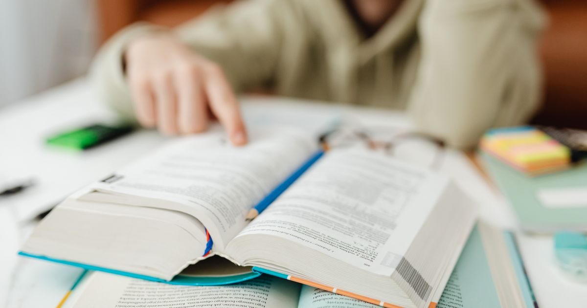 A person pointing at an open book on a desk, focusing on learning.