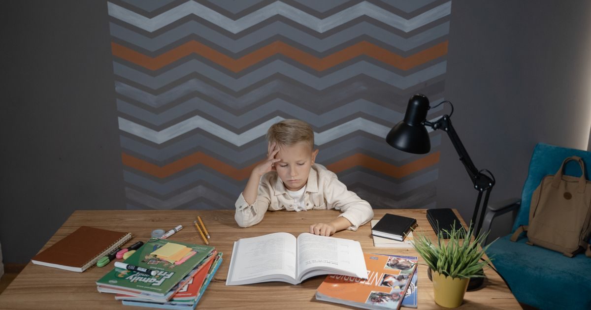 A young boy sitting at a desk, focused on his homework surrounded by school supplies.