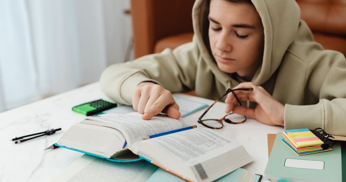 A teenager in a hoodie studying with books and notes on a table, focused on learning indoors.