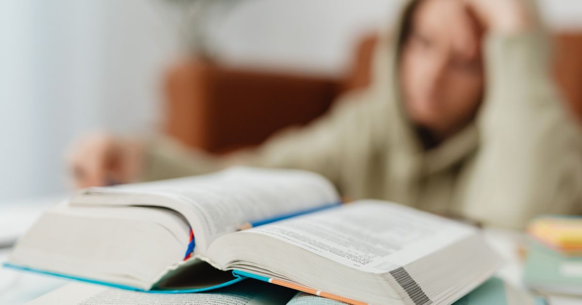 Blurred student studying at desk with open books, showcasing academic stress.