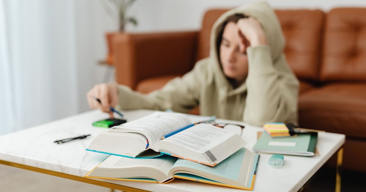Teenager focused on studying with open books and notes on a living room table, capturing a study session.