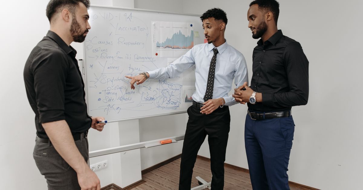 Three professionals discussing strategies at a whiteboard in an office setting.