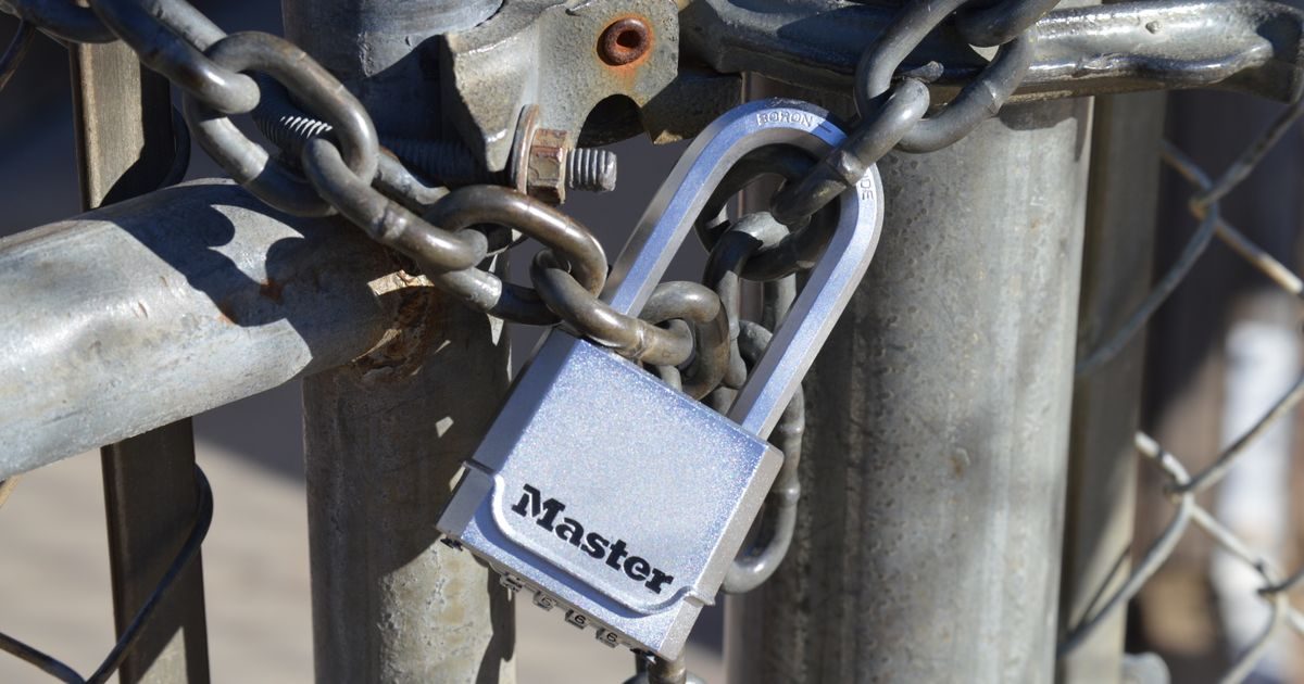 Detailed view of a padlock securing a metal gate with a chain, emphasizing safety and security.